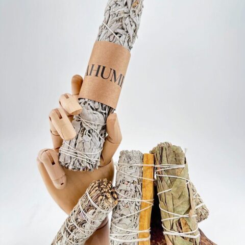 Smudge sticks and wooden hand artfully arranged on driftwood for spiritual cleansing and aromatherapy.