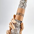 Wooden mannequin hand holds dried sage bundle wrapped and labelled for smudging rituals.