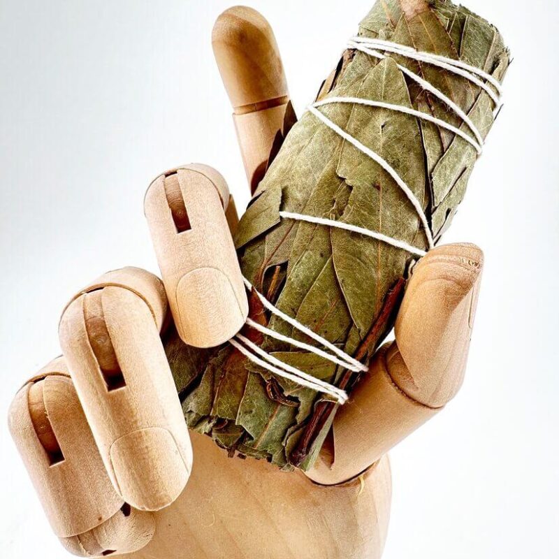 Smudge Stick Wooden mannequin hand holding dried eucalyptus and sage leaves bundle with string on white background.