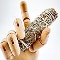 Wooden mannequin hand holding dried sage bundle, contrasting textures, natural artistry.