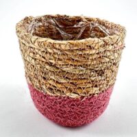 Handmade rustic basket with straw fibres, red dye, and plastic lining for decor or plants.