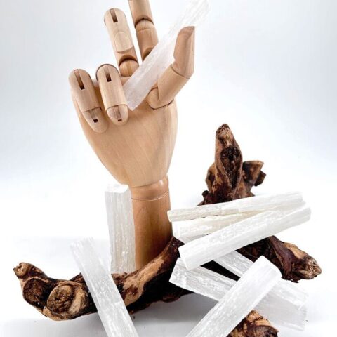 Wooden mannequin hand holding selenite crystal, surrounded by driftwood, emphasising natural and crafted beauty.
