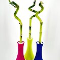 Vibrant bamboo in colourful vases against a minimalist white background, showcasing modern decor.