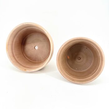 Two terracotta plant pots with drainage holes on white background.