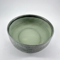 Artisan bowl in muted green with textured exterior and glossy interior, perfect for decor and use.