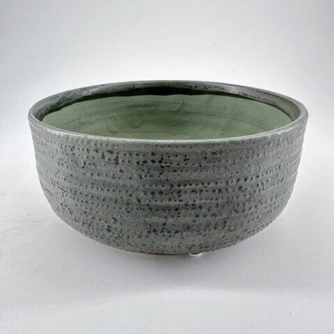 Elegant gray ceramic bowl with textured exterior and soft green interior glaze, perfect for decor.