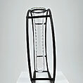 Elegant glass test tube in a minimalist black metal frame on a white pedestal.