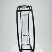 Elegant glass test tube in a minimalist black metal frame on a white pedestal.