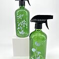 Elegant green glass spray bottles with botanical designs against a white background.