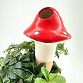 Whimsical red mushroom sculpture nestled among lush greenery, perfect for garden decor or planters.