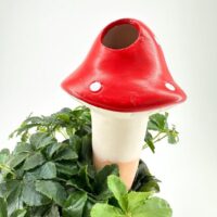 Whimsical red mushroom sculpture nestled among lush greenery, perfect for garden decor or planters.