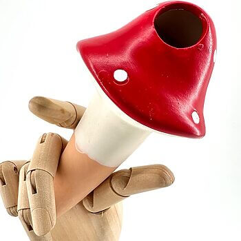 Wooden mannequin hand holding a vibrant red mushroom with white dots against a bright background.