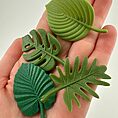 Hand holding green decorative silicone leaves with tropical and monstera designs.