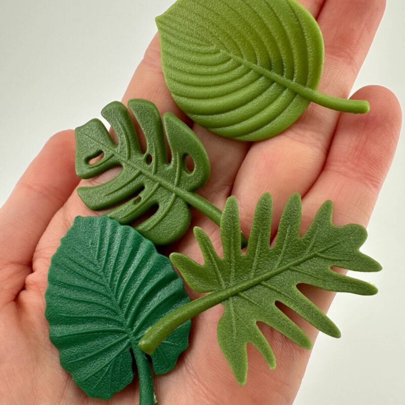 Vibrant Green Silicone Leaf Art in Hand Hand holding green decorative silicone leaves with tropical and monstera designs.