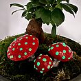 Miniature scene: indoor plant with whimsical red mushrooms in a grey pot.