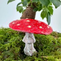 Vivid red fairy-tale mushroom on green moss with indoor plant background.