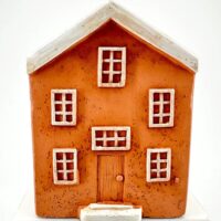 Miniature rustic orange house model with textured exterior and white roof on neutral background.