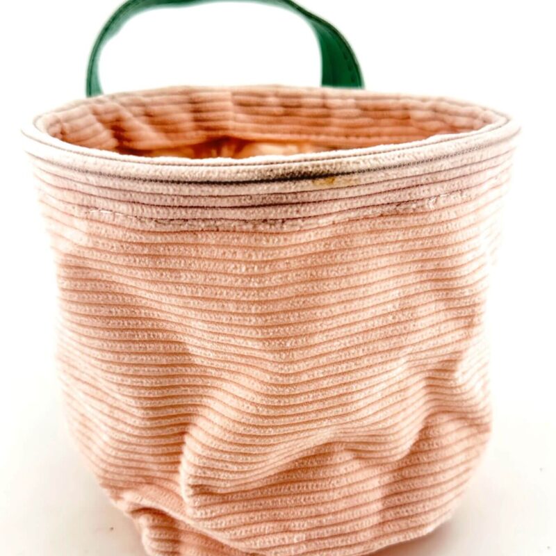 Charming Pink Fabric Basket with Green Handle Pastel pink storage basket with green handle, featuring vertical stripes and cosy, textured fabric.