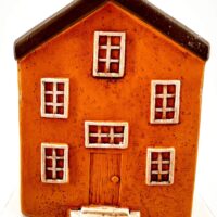 Charming miniature orange house figurine with rustic details and contrasting white framed windows.