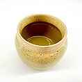 Rustic yellow ceramic pot with speckled texture, glossy interior, and dark liquid.