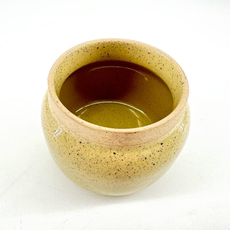 Rustic Yellow Ceramic Pot with Glossy Interior Rustic yellow ceramic pot with speckled texture, glossy interior, and dark liquid.