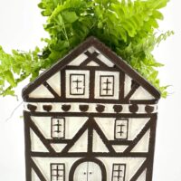 Charming half-timbered house planter with vibrant green ferns for cosy home decor.