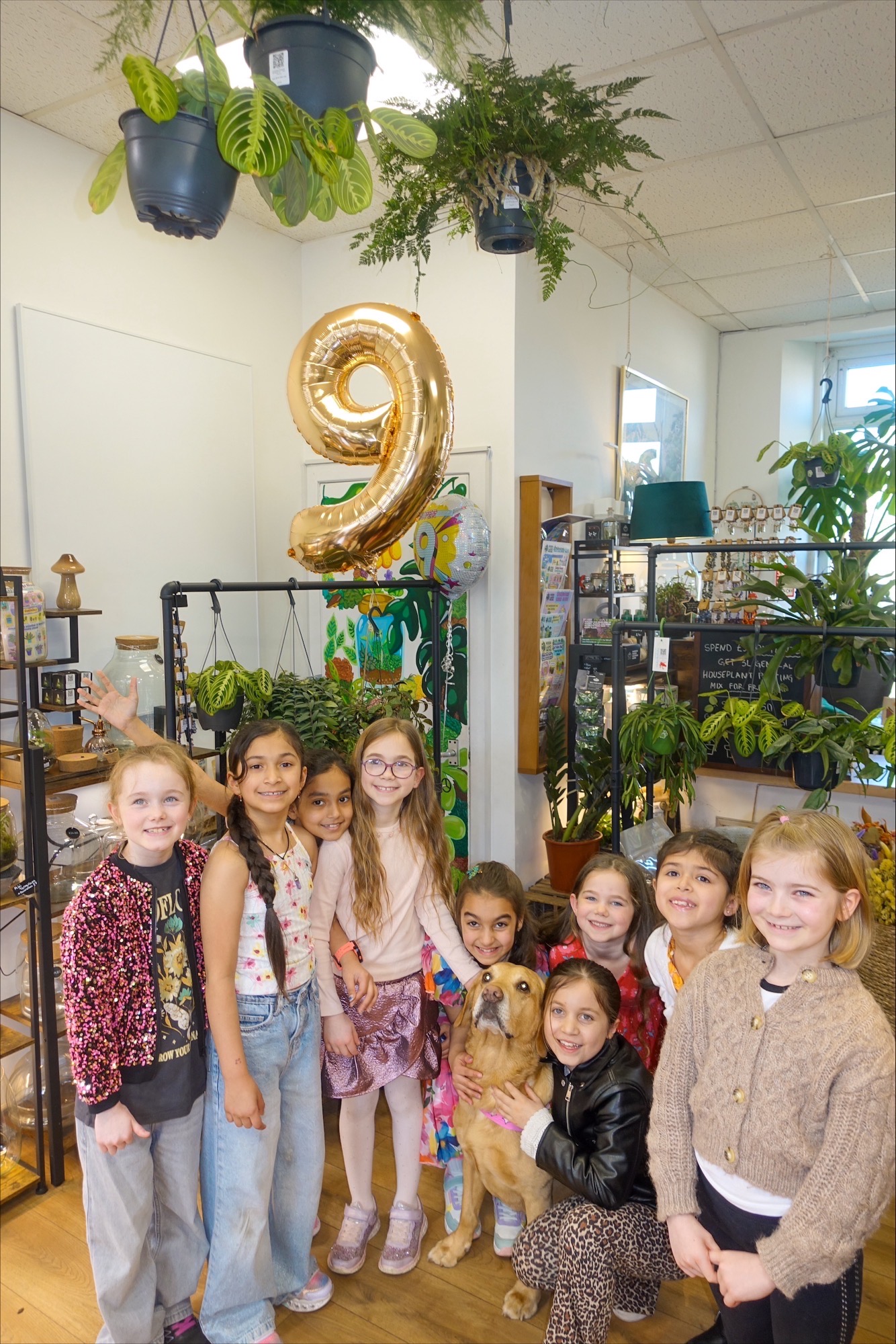 Nine-year-olds birthday party with friends, dog, and greenery in a plant shop setting.