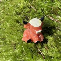 Cartoon cow figurine on vibrant moss, dappled sunlight creates playful forest scene.