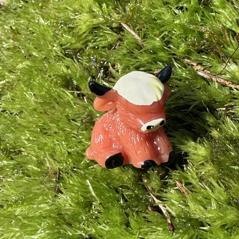 Cartoon cow figurine on vibrant moss, dappled sunlight creates playful forest scene.