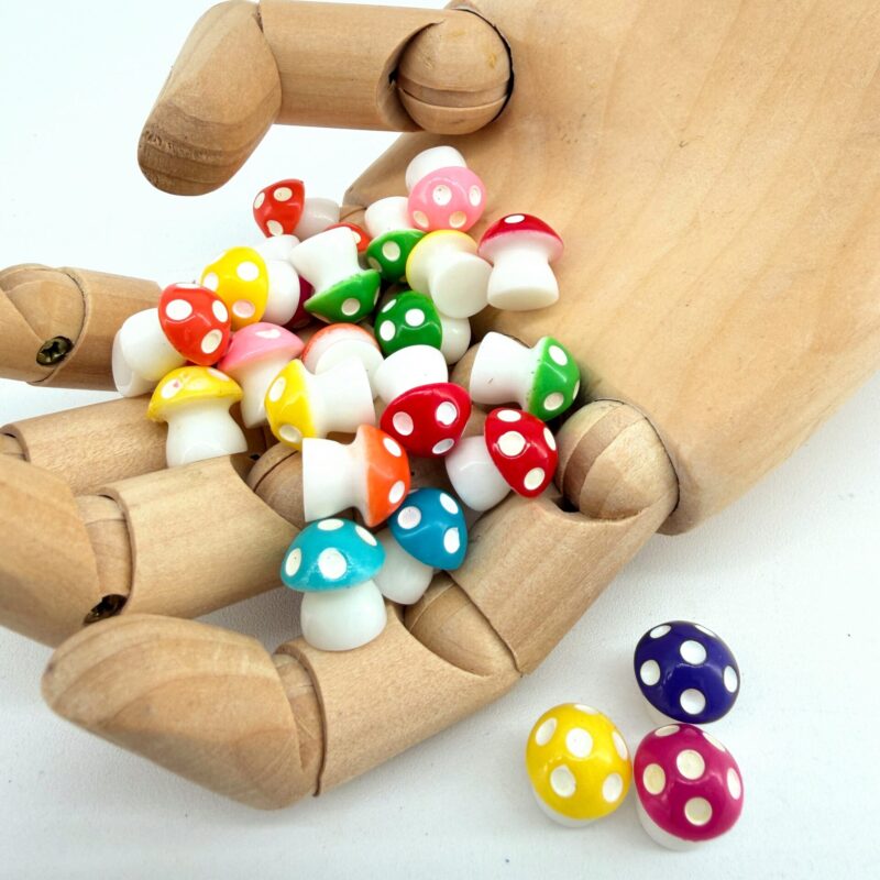 A wooden hand holding a handful of bright mini mushroom decorations with three mushrooms placed beside it.