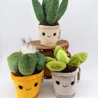 Three cute kawaii plant plush collectables in smiling fabric pots, including cactus and leafy plant designs.
