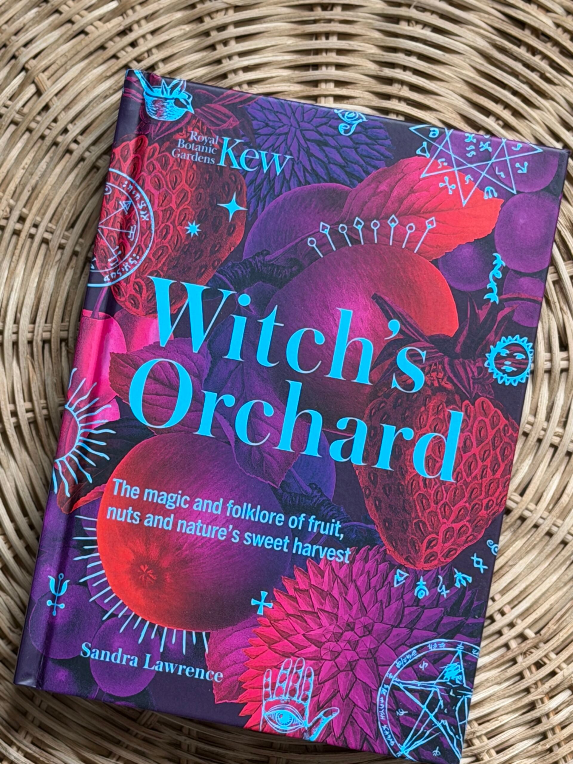Witch’s Orchard by Sandra Lawrence hardback book on a natural woven rattan background.