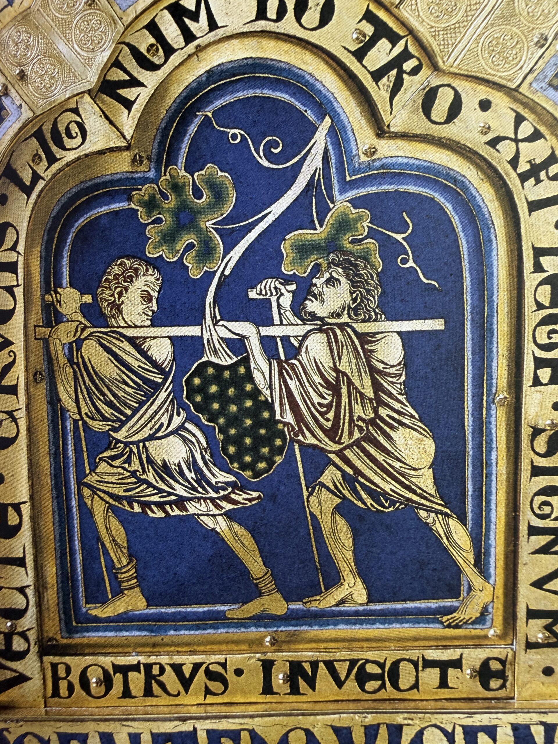 Medieval artwork showing two figures carrying and harvesting a large bunch of grapes.