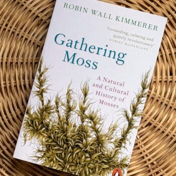 Gathering Moss by Robin Wall Kimmerer paperback book displayed on a natural woven rattan background.